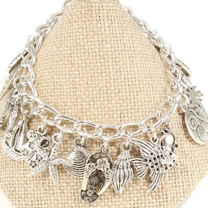 May include: Silver charm bracelet with a variety of nautical themed charms, including a sailboat, starfish, seashells, and a fish.