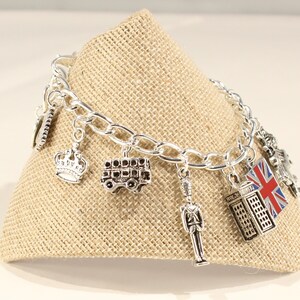 May include: A silver charm bracelet with various London-themed charms, including a crown, a double-decker bus, a telephone booth, a Union Jack flag, and a toy soldier.