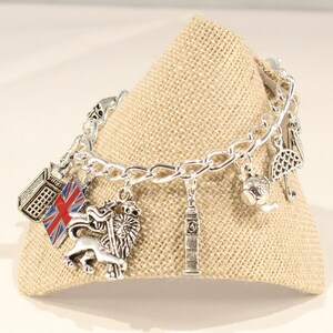 May include: Silver charm bracelet with London themed charms, including a red, white, and blue Union Jack flag, a lion, Big Ben, a building, a teapot, and an umbrella.