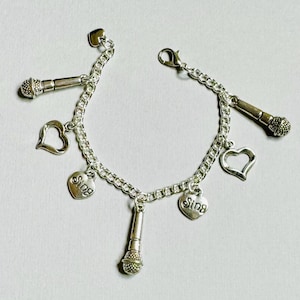 May include: Silver charm bracelet with multiple charms, including two heart charms with the word "Sing" on them, two microphone charms, and a heart charm with an open design.