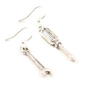 May include: Silver earrings with a wrench and screwdriver charm. The earrings are silver and have a simple design.