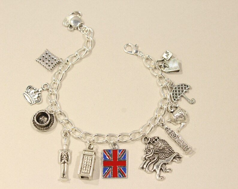 May include: A silver charm bracelet with various charms representing London, England. The charms include a crown, a teacup, a phone booth, a Union Jack flag, a red double-decker bus, a soldier, a lion, and an umbrella.