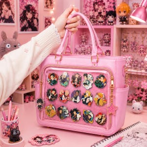 Può includere: Una borsa rosa con un pannello frontale trasparente che mostra spille di personaggi colorati. La borsa ha un manico superiore, una chiusura con cerniera e un ciondolo a forma di stella. Lo sfondo include decorazioni a tema anime.
