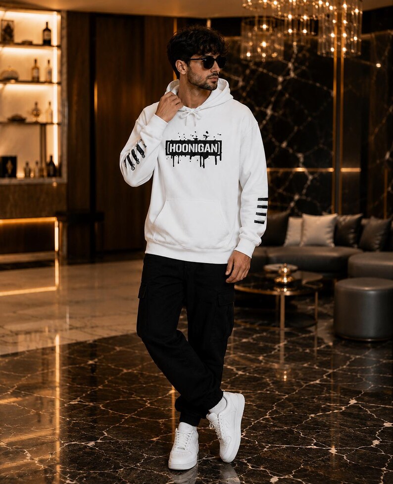 May include: A white hooded sweatshirt featuring a black graphic print on the chest that reads HOONIGAN inside a rectangular box with paint drip effects. The sleeves have black horizontal stripes, and the garment includes a front kangaroo pocket.