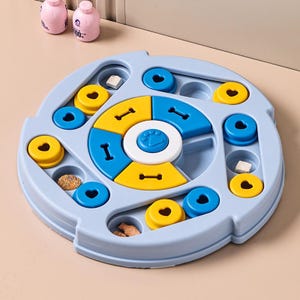 May include: A light blue dog puzzle toy with yellow, blue, and white elements. The toy features compartments and sliding parts for treats. Two pink bottles are visible in the background.