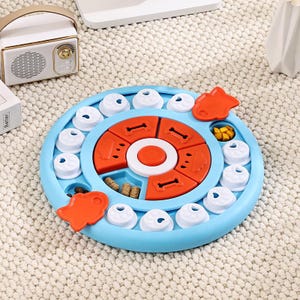 May include: A blue and orange dog puzzle toy with multiple compartments and sliding pieces. The toy features a circular design with various shapes and compartments for treats, promoting mental stimulation for pets.
