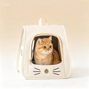Könnte beinhalten: Eine cremefarbene Katzentragetasche mit einem transparenten Frontfenster, das ein Cartoon-Katzen-Gesicht zeigt. Eine orangefarbene Tabby-Katze befindet sich im Inneren. Die Tasche hat einen Griff und einen Reißverschluss.