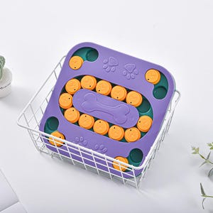 May include: A purple dog puzzle toy with orange circular pieces and a bone-shaped centre. The toy has paw print designs and is inside a white wire basket. The toy is designed to stimulate a dog's mind.