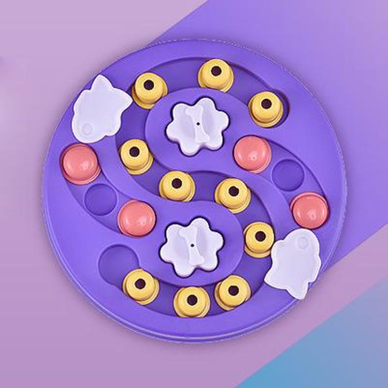 May include: A purple pet puzzle toy with a circular design. It features yellow and pink pieces, along with white flower and fish-shaped elements. The toy is designed to stimulate a pet's mind and provide entertainment.