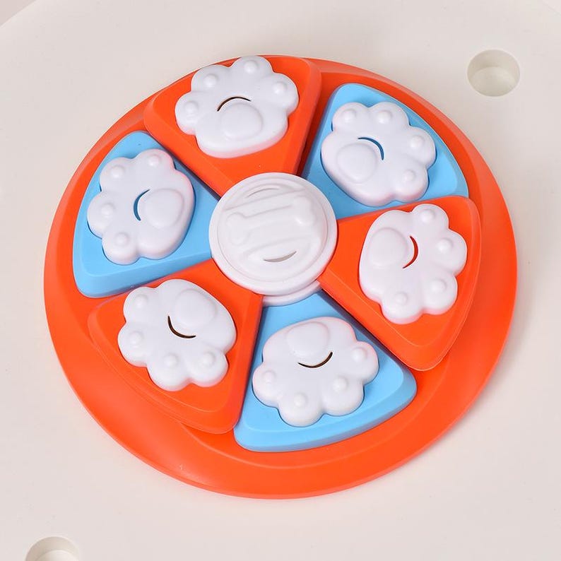 May include: A dog puzzle toy in a circular design with orange, blue, and white components. It has paw-shaped compartments and a central disc. This interactive toy is designed to stimulate a pet's mind.