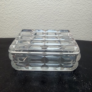 May include: A rectangular clear glass box featuring a geometric pattern of raised heart shapes across the lid and sides. The glass is transparent and faceted, creating a textured surface with repeating heart motifs throughout the entire exterior.