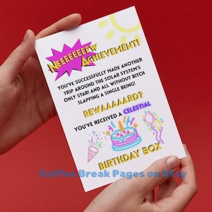 May include: A white rectangular greeting card featuring a pink comic-style burst with the text NEEEEEEEW ACHIEVEMENT! and black text stating YOU'VE SUCCESSFULLY MADE ANOTHER TRIP AROUND THE SOLAR SYSTEM'S ONLY STAR! AND ALL WITHOUT BITCH SLAPPING A SINGLE BEING! REWAAAAARD? YOU'VE RECEIVED A CELESTIAL BIRTHDAY BOX, accompanied by colorful illustrations of a birthday cake, confetti, and balloons.