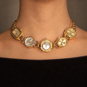 May include: A gold-toned necklace constructed from five distinct vintage watch faces linked together. The watch faces vary in shape, including square, round, and floral-inspired designs, all featuring metallic dials and hands on a chain link base.