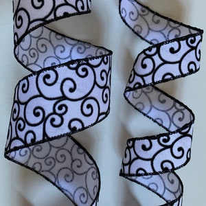 May include: Black and white ribbon with a swirling pattern. The ribbon has a black edge and is made of a soft fabric.