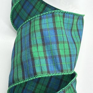 May include: Green, blue, and black plaid ribbon with a wired edge. The ribbon is folded in a spiral shape.