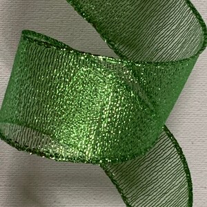 May include: Close-up of a vibrant green ribbon with a shimmering, glittery texture. The ribbon is curled, showcasing its width and the intricate weave of the material. The edges are neatly finished, adding to its decorative appeal.