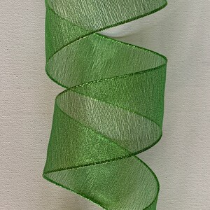 May include: A roll of bright green ribbon with a shimmering, textured surface. The ribbon is spiraled, showcasing its metallic sheen and the delicate texture of the material. The edges are finished with a thin, metallic trim.