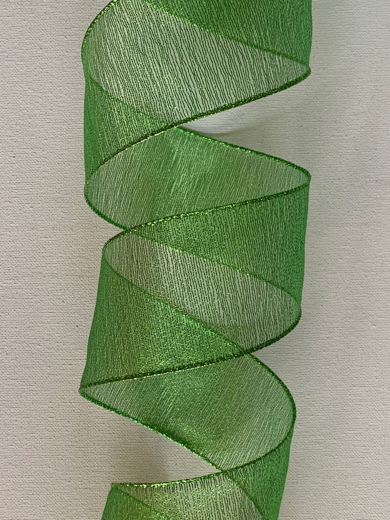 May include: A roll of bright green ribbon with a shimmering, textured surface. The ribbon is spiraled, showcasing its metallic sheen and the delicate texture of the material. The edges are finished with a thin, metallic trim.