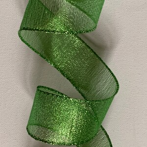 May include: A close-up of a vibrant green ribbon with a shimmering, glittery texture. The ribbon is curled in a spiral shape, showcasing its decorative potential. The edges are neatly finished, adding to its polished appearance. Ideal for crafts and gift wrapping.
