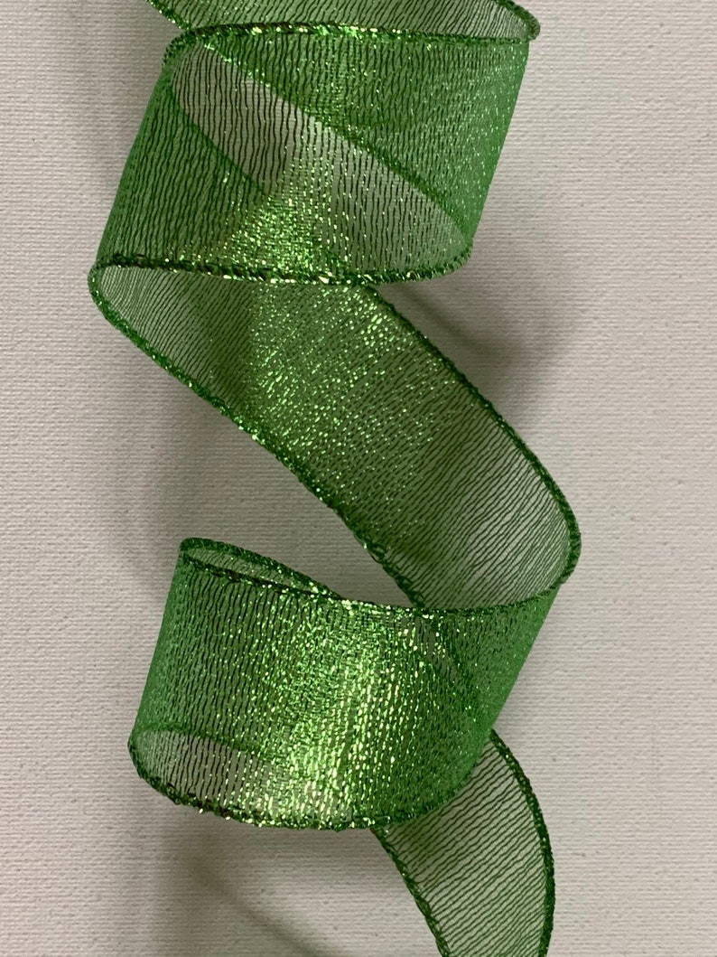 May include: A close-up of a vibrant green ribbon with a shimmering, glittery texture. The ribbon is curled in a spiral shape, showcasing its decorative potential. The edges are neatly finished, adding to its polished appearance. Ideal for crafts and gift wrapping.