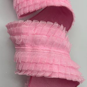 May include: Pink ruffled trim ribbon. The ribbon is made of a sheer, delicate fabric and has a soft, flowing texture.