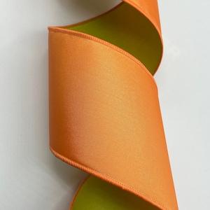 May include: Orange and lime green double-faced satin ribbon. The ribbon is folded and curled, showing both sides.