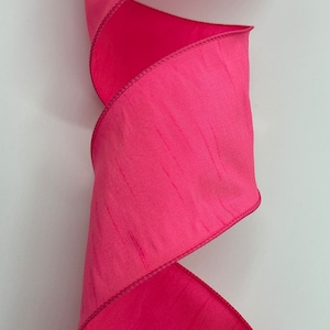 May include: A pink satin ribbon with a subtle shimmer. The ribbon is folded and has a wired edge.