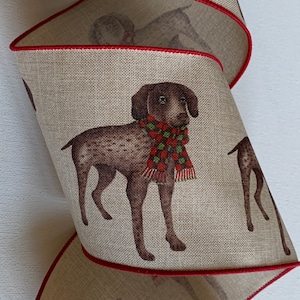 May include: A brown and white dog wearing a red and green scarf is printed on a beige ribbon with a red edge. The ribbon is rolled up and the dog is visible on multiple layers of the ribbon.