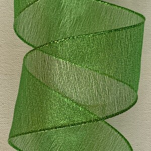 May include: A roll of bright green ribbon with a metallic sheen. The ribbon is spiraled, showcasing its texture and the subtle sparkle of the material. The edges are finished with a thin, metallic trim.