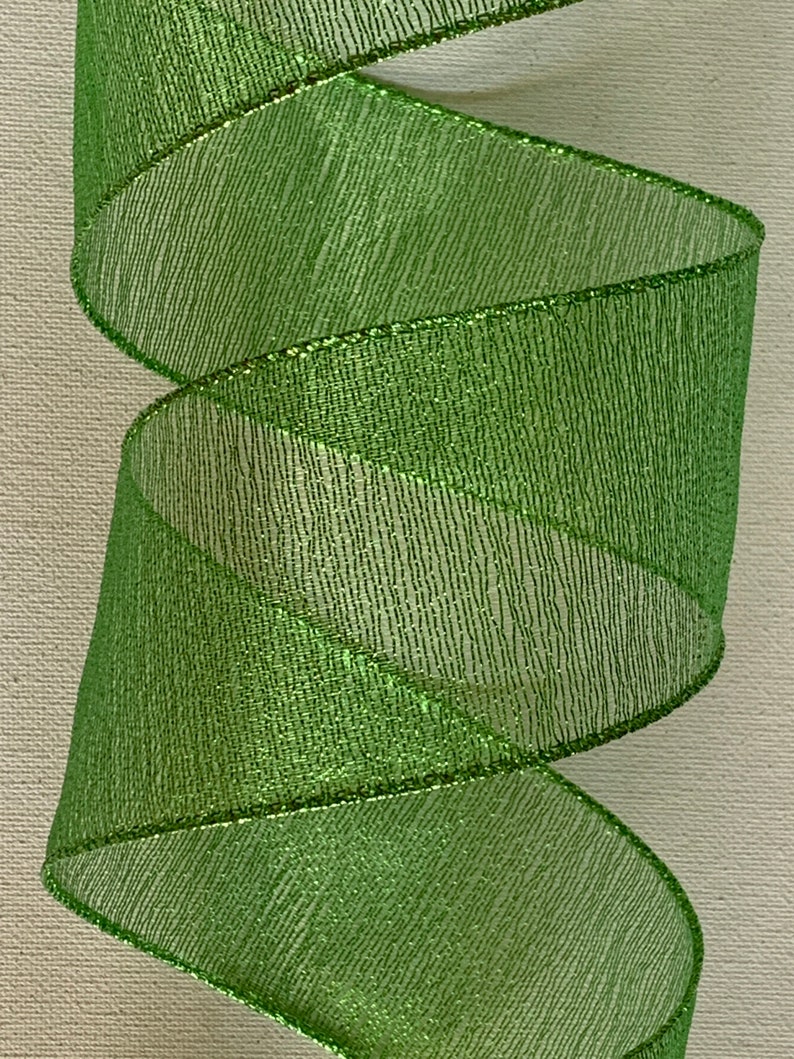 May include: A roll of bright green ribbon with a metallic sheen. The ribbon is spiraled, showcasing its texture and the subtle sparkle of the material. The edges are finished with a thin, metallic trim.