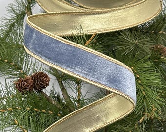 May include: A decorative ribbon with a blue velvet top and gold underside, edged with gold trim. The ribbon is spiraling over a bed of green pine needles and pine cones, creating a festive holiday theme.