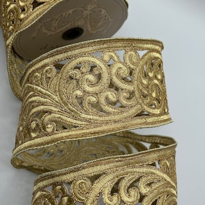 May include: Gold metallic ribbon with a delicate, intricate, floral design. The ribbon is rolled up on a spool.