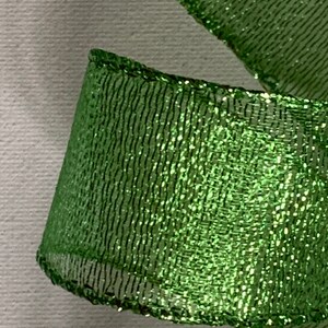 May include: Close-up of a vibrant green ribbon with a shimmering, glittery texture. The ribbon has a mesh-like pattern and is slightly curled, revealing its edges. Ideal for crafting and gift wrapping.
