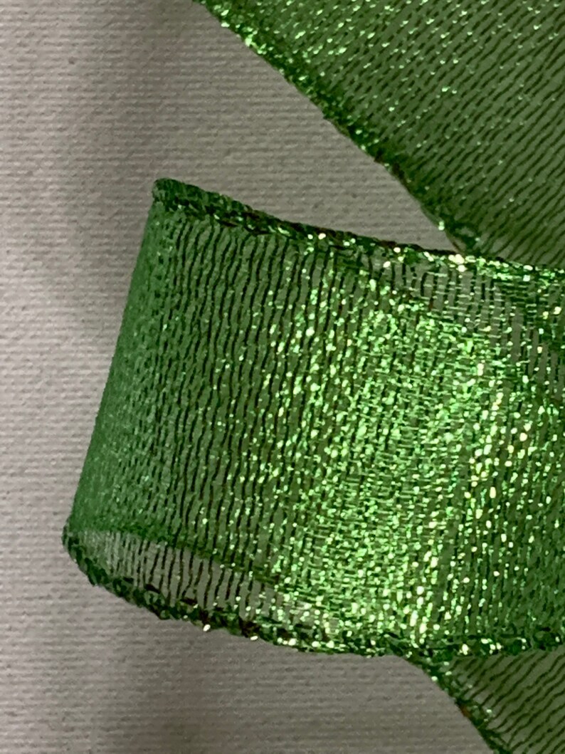 May include: Close-up of a vibrant green ribbon with a shimmering, glittery texture. The ribbon has a mesh-like pattern and is slightly curled, revealing its edges. Ideal for crafting and gift wrapping.