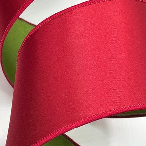 May include: A close-up of a red satin ribbon with a green underside. The ribbon is tightly curled, showcasing the texture and sheen of the fabric. The edges are neatly stitched, adding a finished look.