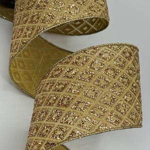 Puede incluir: Primer plano de una cinta dorada con un patr&oacute;n de diamantes y detalles brillantes. La cinta est&aacute; enrollada, revelando ambos lados del material. Los bordes est&aacute;n adornados con un borde dorado. Esta cinta decorativa es adecuada para manualidades y envolver regalos.