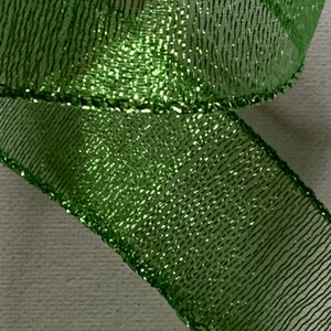 May include: Close-up of a shimmering green ribbon. The ribbon has a mesh-like texture with a glittery sheen, creating a sparkling effect. The edges are neatly finished, and the ribbon is slightly curled, suggesting it's part of a decorative item.