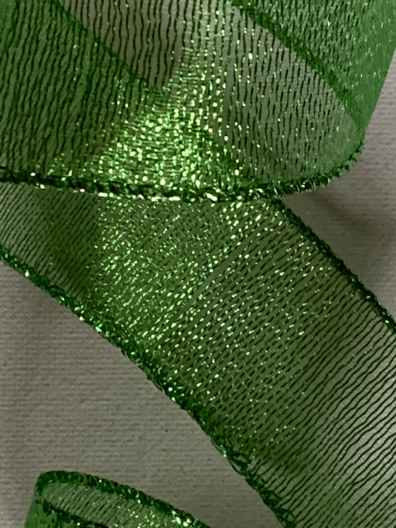May include: Close-up of a shimmering green ribbon. The ribbon has a mesh-like texture with a glittery sheen, creating a sparkling effect. The edges are neatly finished, and the ribbon is slightly curled, suggesting it's part of a decorative item.
