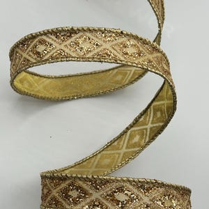 Puede incluir: Cinta dorada con un patr&oacute;n de diamantes y detalles brillantes. La cinta est&aacute; enrollada, mostrando su dise&ntilde;o y textura. Los bordes est&aacute;n adornados con un detalle dorado en forma de cuerda. Adecuada para manualidades y envolver regalos.