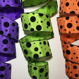 May include: Three rolls of black and white polka dot ribbon. The ribbon is available in purple, green, and orange.