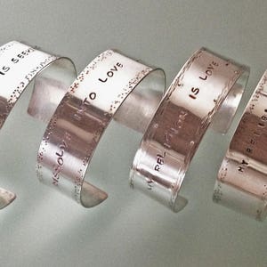 May include: Seven silver bracelets with engraved text. The text on the bracelets reads "To Love Is Grey", "My Love Is Law", "What You Give Is What You Get", "My Love Is Grey", "To Love Is Grey", "My Love Is Law", and "What You Give Is What You Get".
