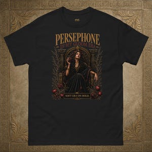 May include: Black t-shirt with a detailed graphic of Persephone. The design includes the text "PERSEPHONE IN MY GLOOM ERA" and "SOFT ERA ON HOLD." The artwork shows a woman in a dark gown, seated on a throne, with ornate details.