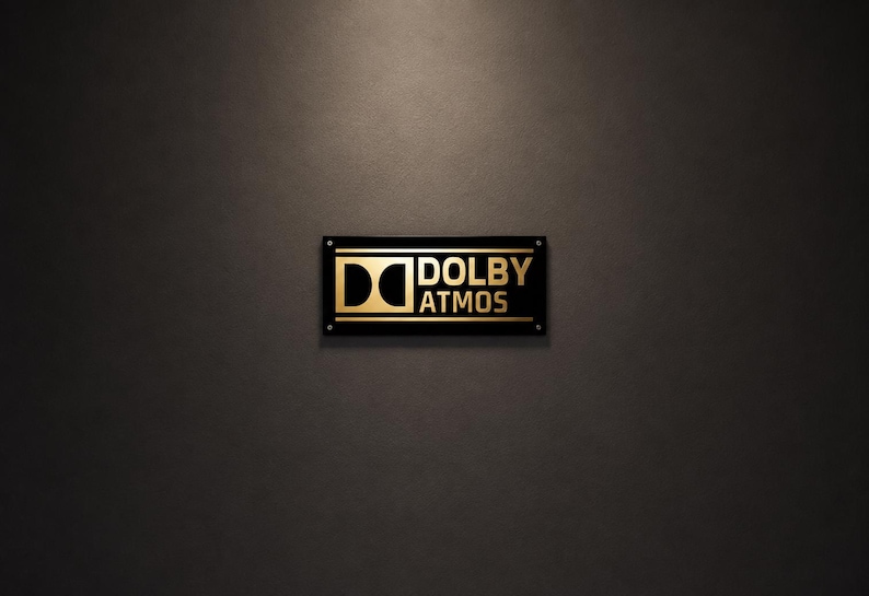 Może przedstawiać: Prostokątny czarny znak ze złotym napisem &bdquo;DOLBY ATMOS&rdquo;. Znak jest zamontowany na ciemnoszarej ścianie. Logo Dolby jest r&oacute;wnież w kolorze złotym.