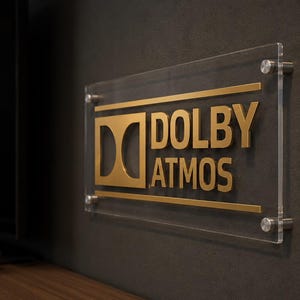 Może przedstawiać: Przezroczysty akrylowy znak z złotymi literami i logo Dolby Atmos. Znak jest zamontowany na ciemnoszarej ścianie ze srebrnym osprzętem. Znak jest prostokątny i ma nowoczesny design.