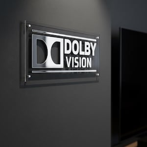 K&ouml;nnte beinhalten: Ein rechteckiges Wand-Schild mit dem Dolby Vision Logo in silberner Metallschrift auf einer transparenten Acrylplatte. Das Schild ist mit vier silbernen Abstandshaltern an den Ecken befestigt und zeigt den Text Dolby Vision.