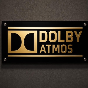 Może przedstawiać: Czarny prostokątny znak z złotym napisem "DOLBY ATMOS". Logo Dolby znajduje się po lewej stronie. Znak jest zamontowany za pomocą czterech srebrnych śrub na ciemnoszarej, teksturowanej powierzchni.