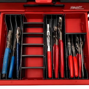 May include: A red Milwaukee Packout tool box drawer with black plastic dividers organizing various metal pliers. The left section holds blue-handled pliers, while the right sections contain multiple pliers with bright red rubberized handles.