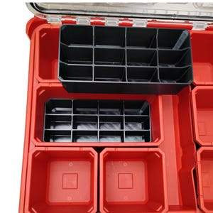 May include: A red plastic tool organizer case featuring a clear lid and multiple internal compartments. The interior contains two black plastic grid inserts with twelve small sections each, alongside several empty red square storage bins.