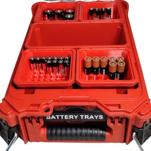 May include: A red plastic battery organizer case with multiple internal compartments. The front features a black label with the white text BATTERY TRAYS. The case contains various cylindrical batteries stored in molded slots within the red trays.