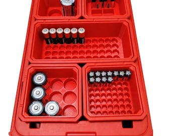 May include: A bright red plastic battery organiser case featuring multiple partitioned compartments. The interior contains various cylindrical and rectangular batteries arranged in rows and circular slots within the moulded grid structure.